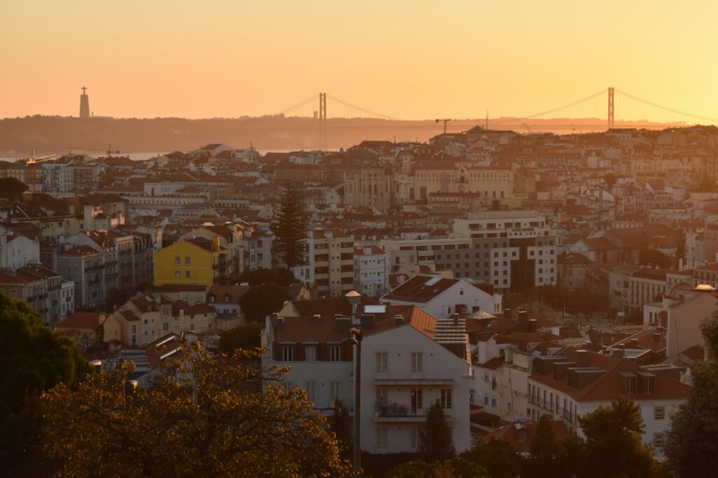 Panoramic sunset view of Lisbon rooftops with 25 de Abril Bridge and Cristo Rei statue from Miradouro da Senhora do Monte Portugal